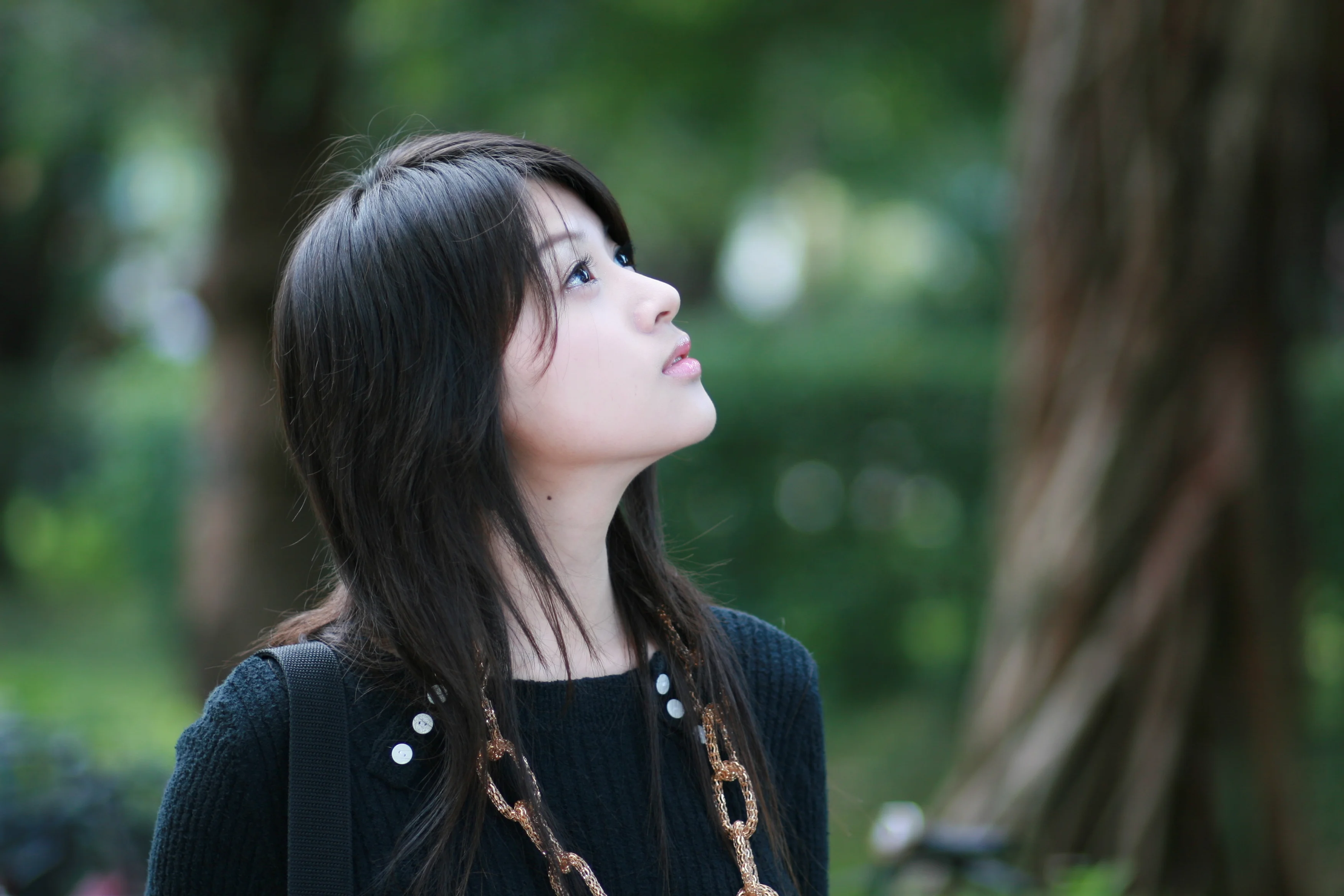 Gái xinh Việt Nam tóc đen dài ngước nhìn lên trong công viên, nền xanh bokeh tuyệt đẹp