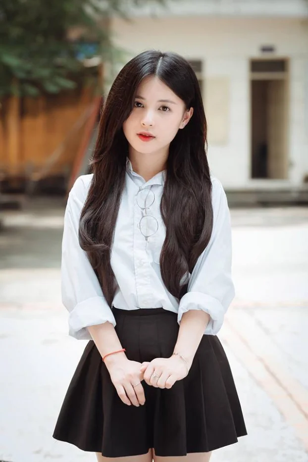 Gái xinh Việt Nam tóc đen dài mặc áo sơ mi trắng váy đen đứng trước sân trường